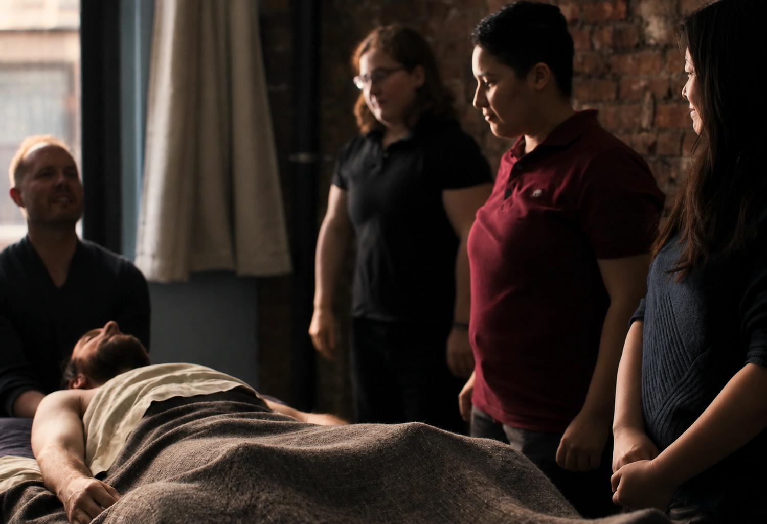 David Weintraub beside a client on the table, talking the treatment through with three Bodyworks DW therapists